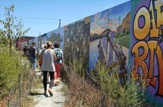 several people walking down a path with graffiti on the wall