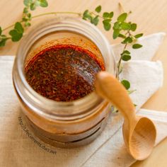 a jar filled with red sauce sitting on top of a white napkin next to a wooden spoon