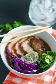 a white bowl filled with meat and veggies on top of a red and white checkered table cloth