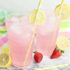 two glasses filled with pink lemonade and strawberries on top of a marble table