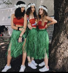 three young women in grass skirts standing next to a tree with their arms around each other