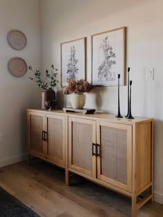 a wooden cabinet with two vases on top of it next to pictures and plants