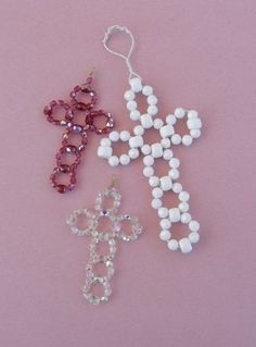 three beaded cross ornament hangings on a pink background, one in white and the other in red