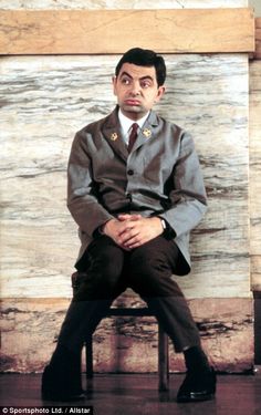 a man sitting on top of a chair in front of a wall with a painting behind him