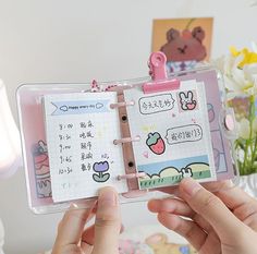 a person holding up a planner book with stickers on the pages and writing in it