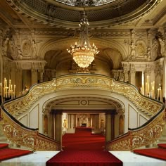 an ornate staircase with red carpet and chandelier in the center, leading to a grand entrance