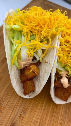 two tacos covered in cheese and lettuce on top of a cutting board