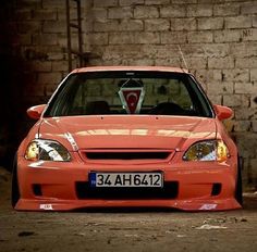 an orange car parked in front of a brick wall with the word duzi jamz written on it