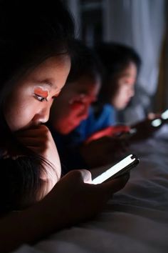 two children are looking at their cellphones in the dark, while one child looks on