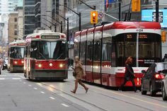 two people crossing the street in front of a red and white bus on a city street