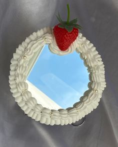 a strawberry on top of a mirror with pearls around the edges and an attached ring