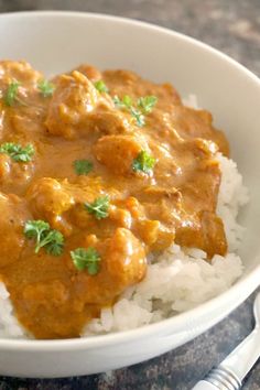 a white bowl filled with rice and meat covered in gravy on top of a table