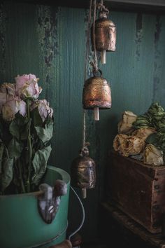 three bells hanging from a green wall next to some flowers and an old wooden box