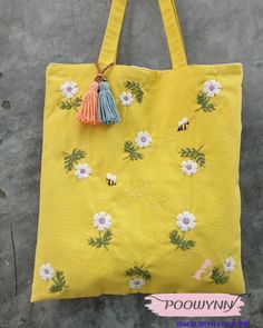 a yellow tote bag with flowers and tassels hanging from the handle on concrete floor