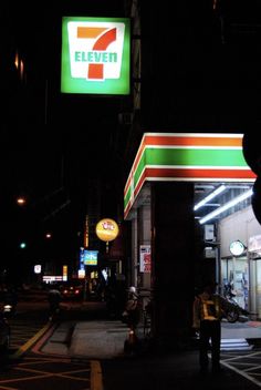 a gas station at night with the 7 eleven sign lit up in green and orange