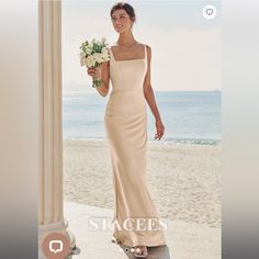 a woman in a long dress is standing on the beach and holding a bouquet of flowers