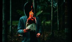 a person with a hoodie on holding a book in the woods while wearing a fire mask