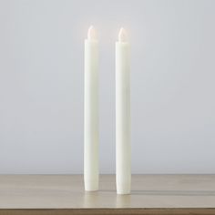 two white candles sitting on top of a wooden table