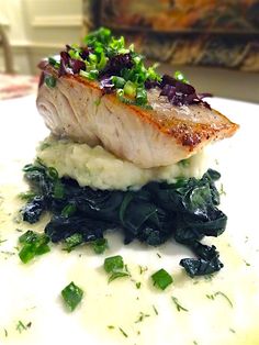 a piece of fish on top of mashed potatoes and greens