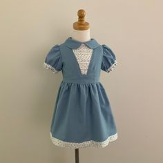 A girls' vintage inspired dress made from soft to the touch cotton. The front bodice features a floral yoke with horizontal pintucks, a v-shaped band above the waist, a classic Peter Pan collar, puff sleeves, and fit and flare skirt with border across the hemline. The back has a button closure for easy dressing and the skirt is lined in cotton poplin. This garment is AU Size 3 and is READY to SHIP. Approximate Garment Measurements: Chest 58 cm (22 7/8 in) Waist 56 cm (22 in) Front Waist Length 2 Spring School Dress With Peter Pan Collar, Fitted Doll Collar Dress For School, Retro Cotton School Dress, Cotton Fitted Dress With Doll Collar, Vintage Dresses For School In Spring, Cute Fitted Cotton Vintage Dress, Fitted Cotton Dresses For Tea Party, Fitted Cotton Vintage Dress With Doll Collar, Cotton Fitted Dress With Peter Pan Collar