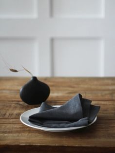 a black vase sitting on top of a wooden table next to a white plate and napkin