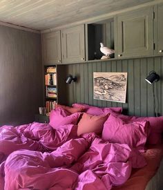 a bed with pink sheets and pillows in a room next to a book shelf filled with books