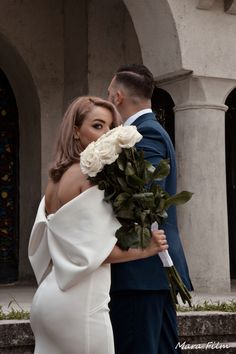 a man in a suit and tie holding a bouquet of flowers next to a woman in a white dress