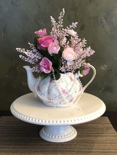 a white tea pot with pink and purple flowers in it on a cake platter