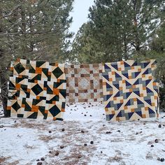 three quilts are hanging in the snow near some trees