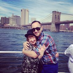 a man and woman hugging each other on a boat in front of the brooklyn bridge