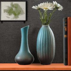 two vases with white flowers in them on a shelf next to books and a bookcase