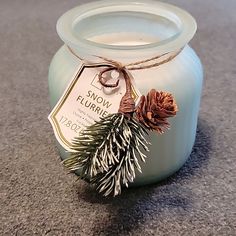 a small jar filled with snow flurries on top of a floor next to a pine cone