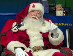 a man dressed as santa claus sitting in front of a microphone and giving a thumbs up