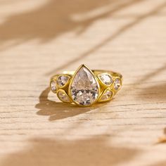 a gold ring with two pear shaped diamonds on it, sitting on a wooden surface