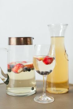 a pitcher of water and a glass with berries in it on a table next to a jug