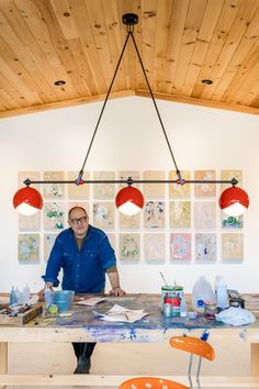 a man is sitting at a table in front of some art work on the wall