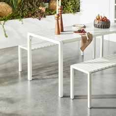 a white table with two benches and a bowl of fruit on the table next to it