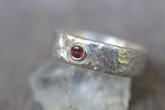 This simple garnet wedding band in sterling silver will be made to order within 10-15 business days. Gift box & polishing cloth included. The ring is approximately 6mm wide with a hammered, shiny finish. The gemstone is a 3mm round faceted natural red garnet in a low profile tube setting. Prefer a different stone? You can choose between any of the stones pictured in photo 8: White Zircon, Sky Blue Topaz, Peridot, London Blue Topaz, Rhodolite Garnet, Amethyst, Lab Created Ruby, Red Garnet, Black Garnet Wedding Band, Tube Setting, Engagement Rings Handmade, Garnet Wedding Rings, Garnet Wedding, Red Spinel, Sterling Silver Wedding Band, Handmade Engagement Rings, Rings Handmade