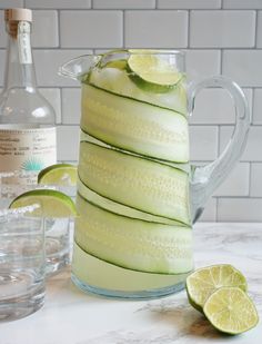 a pitcher filled with cucumber and limes next to two glasses on a counter