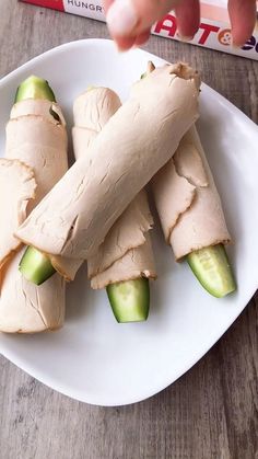 a plate with cucumber wrapped in bread on it and someone reaching for something