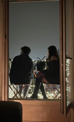 two people sitting in chairs looking out at the city lights from an apartment building's balcony