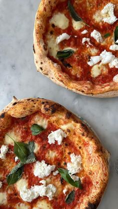 two pizzas sitting on top of a white countertop covered in cheese and basil