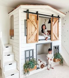 two children are sitting on the roof of a doll house with wooden doors and windows