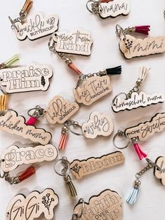 wooden keychains with names and phrases are arranged on a white surface, including one that has a tassel in the middle