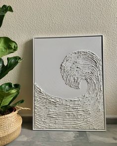 a plant is sitting next to a white framed art piece on a table with a potted plant in front of it