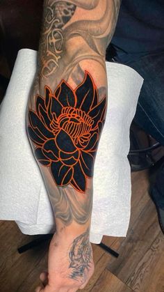 a man's arm with an orange and black flower tattoo on his left arm