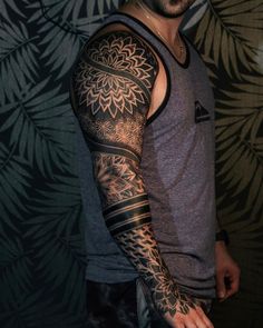 a man with a tattoo on his arm and shoulder is standing in front of a wall