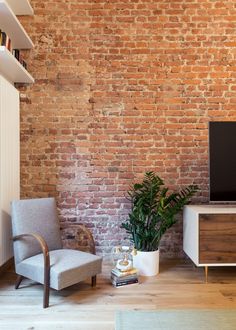 a living room with a brick wall and wooden flooring, two chairs, a television on a stand and a plant in a pot