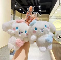 two white stuffed animals are held up by someone's hand