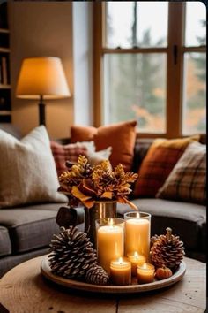 candles and pine cones sit on a tray in front of a couch